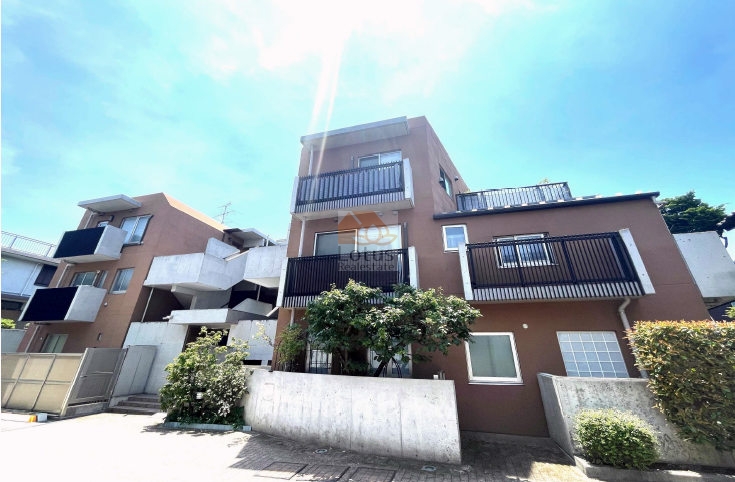 第一種住居専用地域に建つ低層RC造の外観で、下高井戸駅徒歩5分の住宅地に穏やかに溶け込む構成です。植栽とバルコニーの配置が視線を分散し、落ち着いた距離感を生みます。