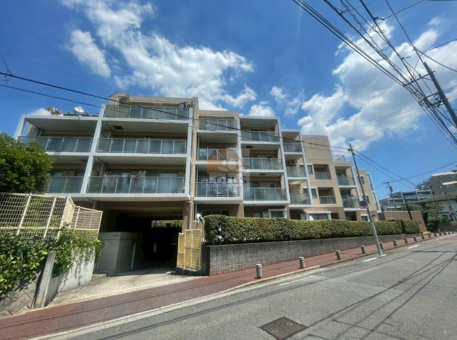 第一種低層住居専用地域に調和する低層4階建の外観で、道路との距離が確保され、車の走行音が抑えられた配置です。ガラス手すりを用いたバルコニーが連なり、2002年築らしい落ち着いた設計といえます。