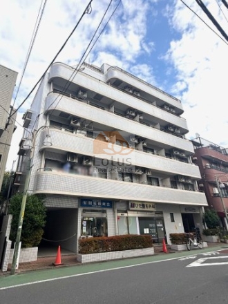 武蔵小山駅徒歩3分の立地に立つ外観は、白を基調としたタイル張りで、角の丸みを帯びたラインが通りにやわらかな印象を与えます。空を広く切り取る上層のバルコニー形状と、1階に店舗が入る構成が、街との距離感をほどよく保つ設計です。昼間は反射光が穏やかに回り、住宅街と商業動線の中間に位置する建物としての性格が伝わってきます。